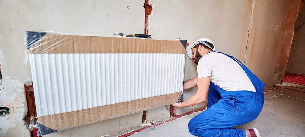 Male plumber in work overalls installing heating radiator in empty room. Young man in safety helmet installing heating system in apartment. Concept of installation, plumbing works and home renovation. 
- © Shutterstock